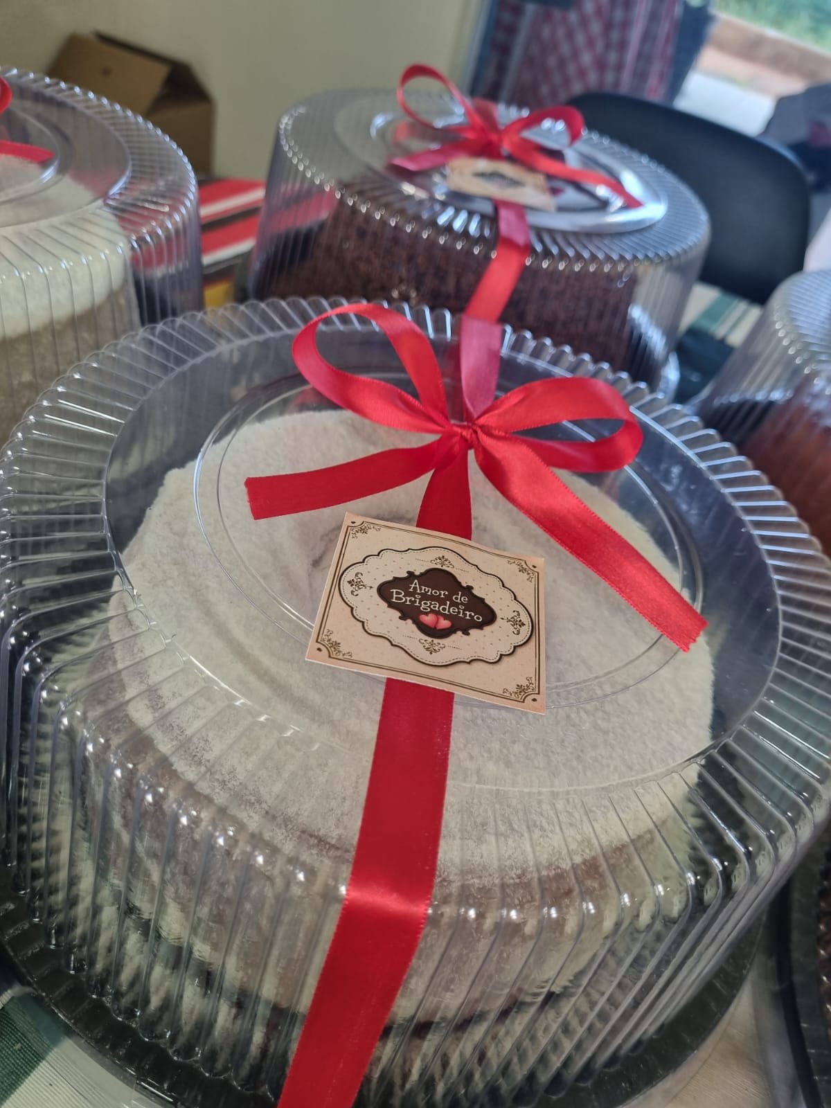 Bolo branco embalado com laço vermelho e cartão Amor de Brigadeiro